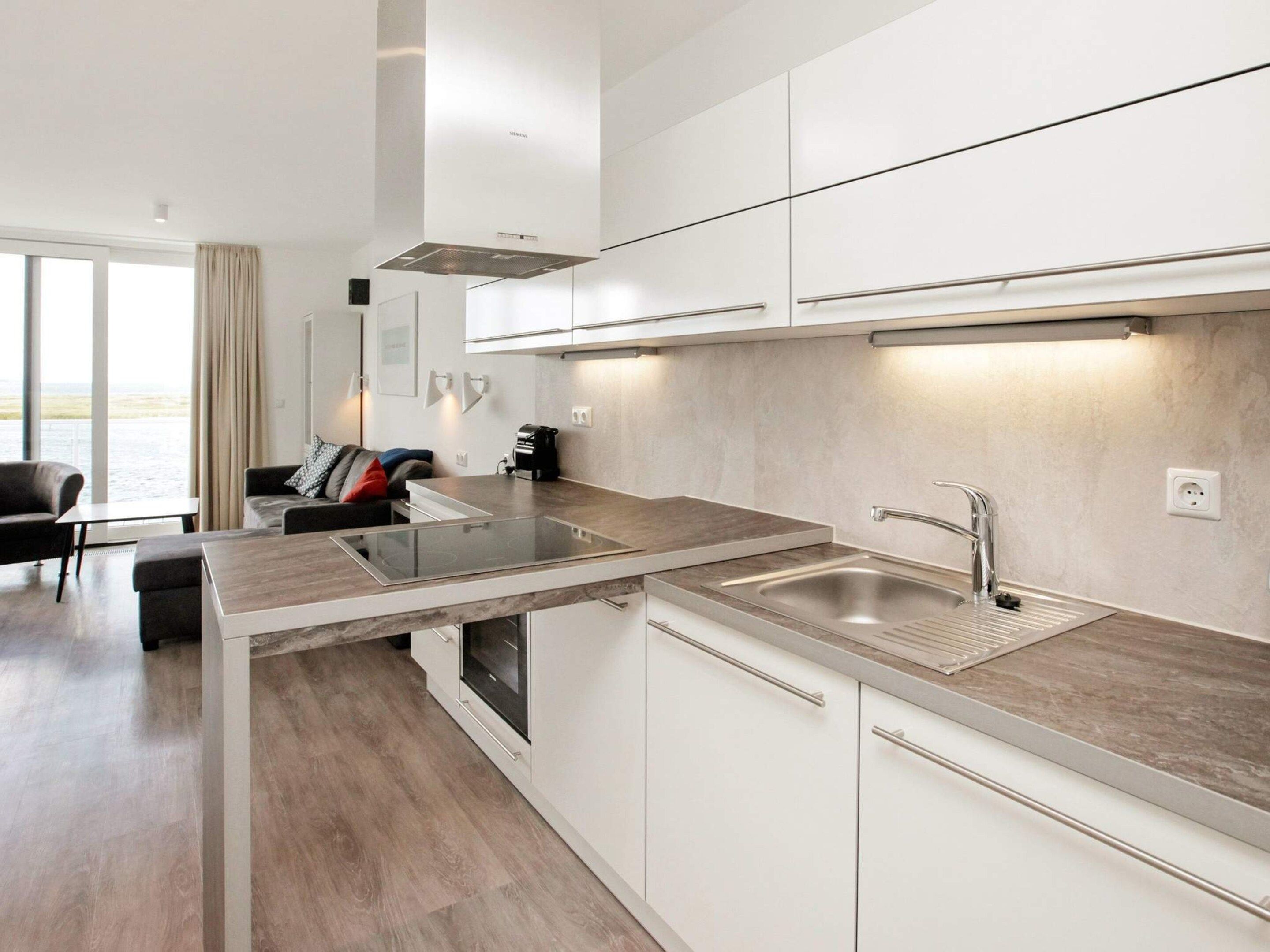 Una cocina moderna con armarios blancos, un lavamanos de acero inoxidable y un horno empotrado.