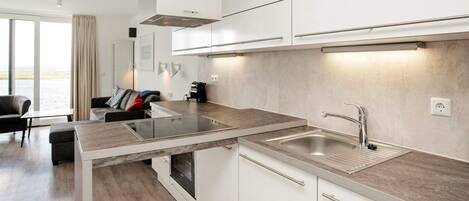 Una cocina moderna con armarios blancos, un lavamanos de acero inoxidable y un horno empotrado.