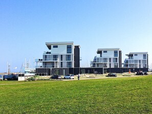 A modern coastal building with multiple floors and balconies, situated on a grassy area with a clear sky. - Holiday Home in Wendtorf (Schönberg)