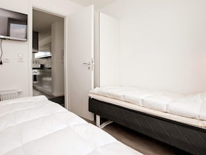 A bedroom with a bed, a bedside table, and a view into a kitchen area. - Holiday Home in Wendtorf (Schönberg)