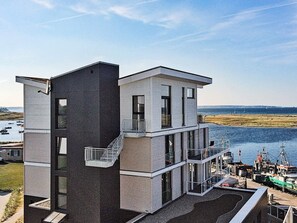 Ein modernes, zweistöckiges Gebäude mit Balkon, großen Fenstern und Blick auf Wasser und Boote.