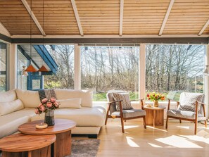 A modern living room with a sofa, two armchairs, a coffee table, and a large window offering a view of trees. - 4 Star Holiday Home in Bindslev (Bindslev)