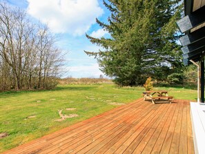 A wooden deck with picnic tables, surrounded by a grassy field and trees. - 4 Star Holiday Home in Bindslev (Bindslev)