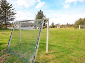 Un but de football sur un terrain herbeux, avec un filet, entouré d’arbres et avec un bâtiment en arrière-plan.