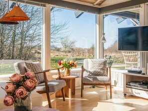 A modern living room with large windows, a television, and a dining area with a table and chairs. - 4 Star Holiday Home in Bindslev (Bindslev)