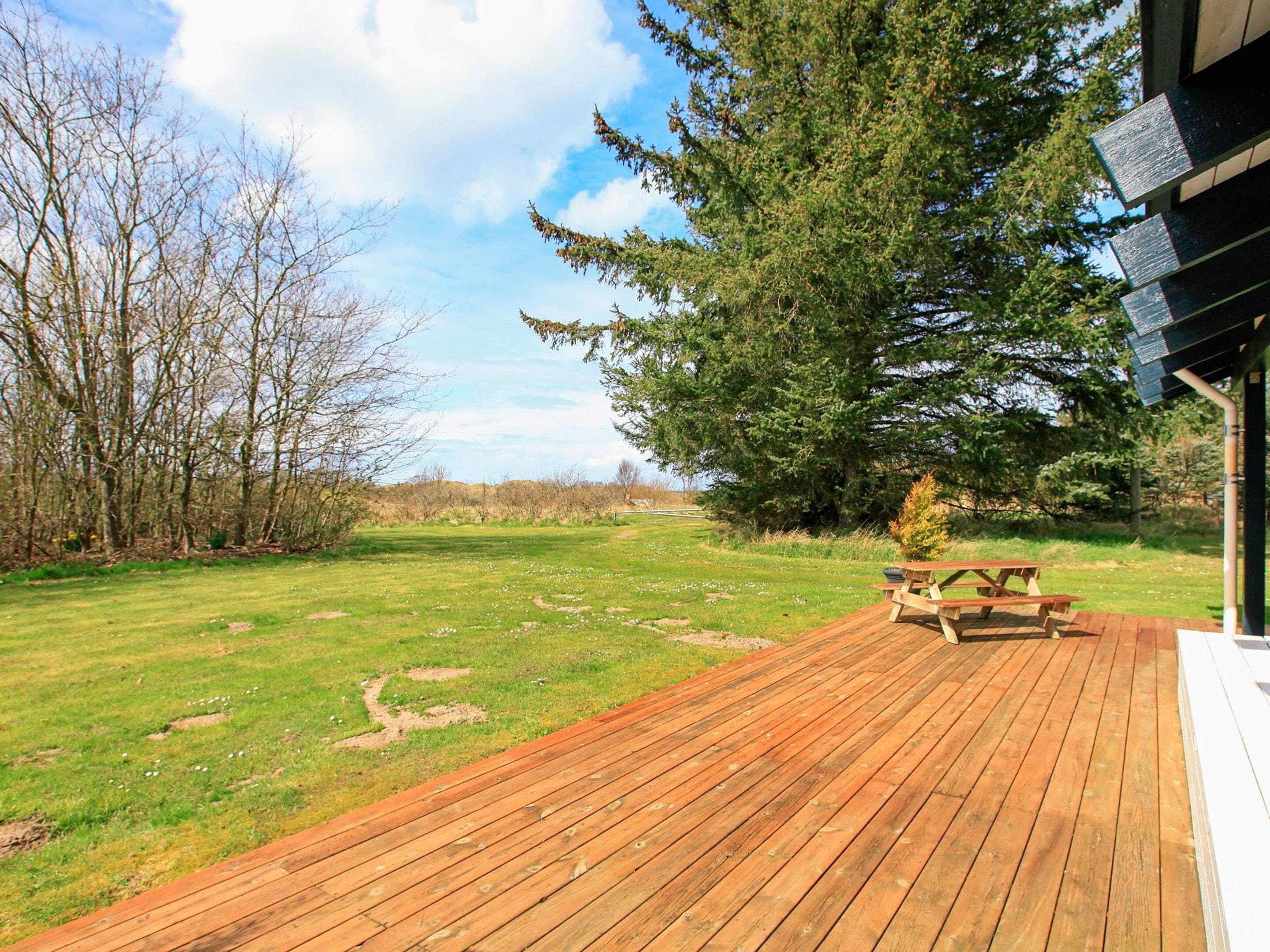 A wooden deck with picnic tables, surrounded by a grassy area and trees.