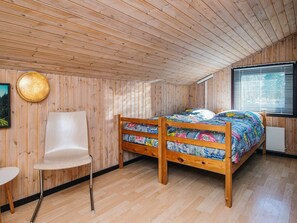 Una habitación con paneles de madera, una cama, una silla y una ventana con persianas.