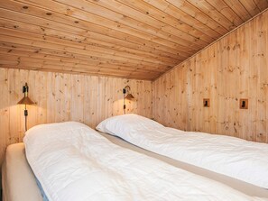 A room with wooden walls and ceiling, two beds with white bedding, and two wall-mounted lamps. - 4 Star Holiday Home in Bindslev (Bindslev)