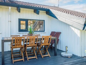 Une terrasse en bois avec une table et des chaises, un pot de fleurs et un chauffage en pierre.