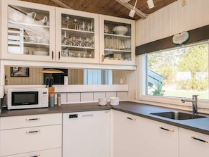 A kitchen with white cabinetry, a built-in microwave, and a window with a view of greenery. - 4 Star Holiday Home in Bindslev (Bindslev)