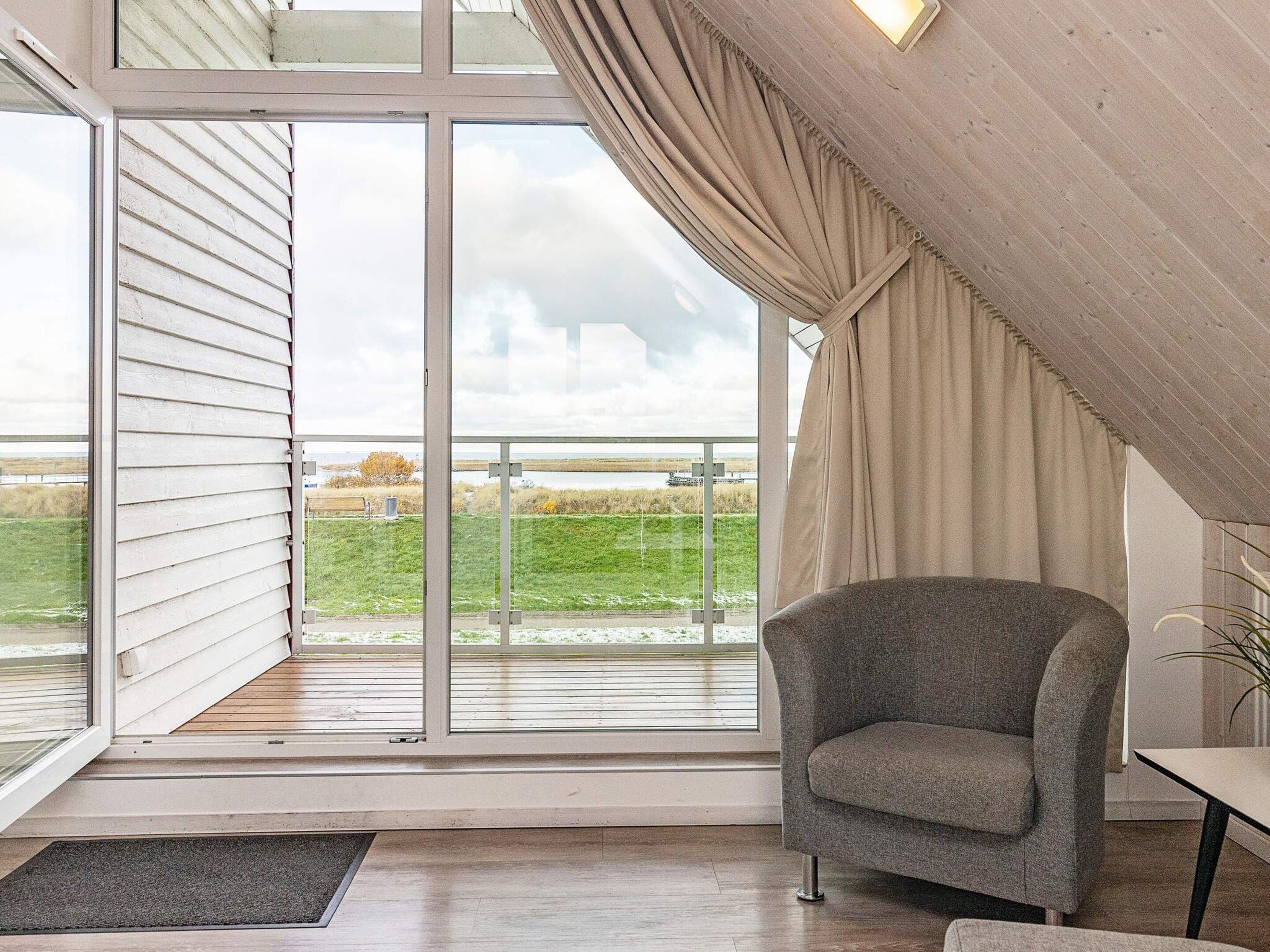 A room with a large sliding glass door leading to a balcony, a grey armchair, and a small table.