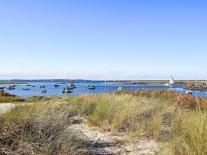 Un paysage côtier avec des bateaux sur l’eau, une jetée où se trouvent des personnes, et un ciel dégagé.