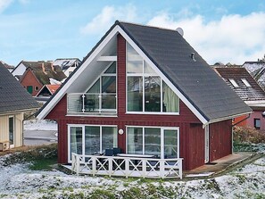 Une maison à deux étages dotée d’un balcon imposant, de grandes fenêtres et d’une façade rouge.