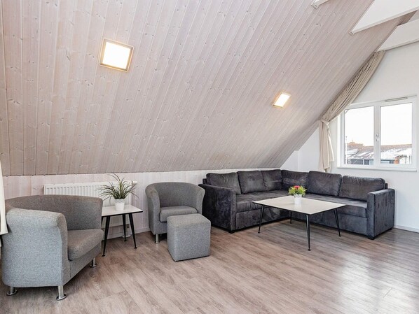 Un espace de vie moderne de style loft, avec un plafond en pente, un canapé d’angle, une petite table et une plante en pot.