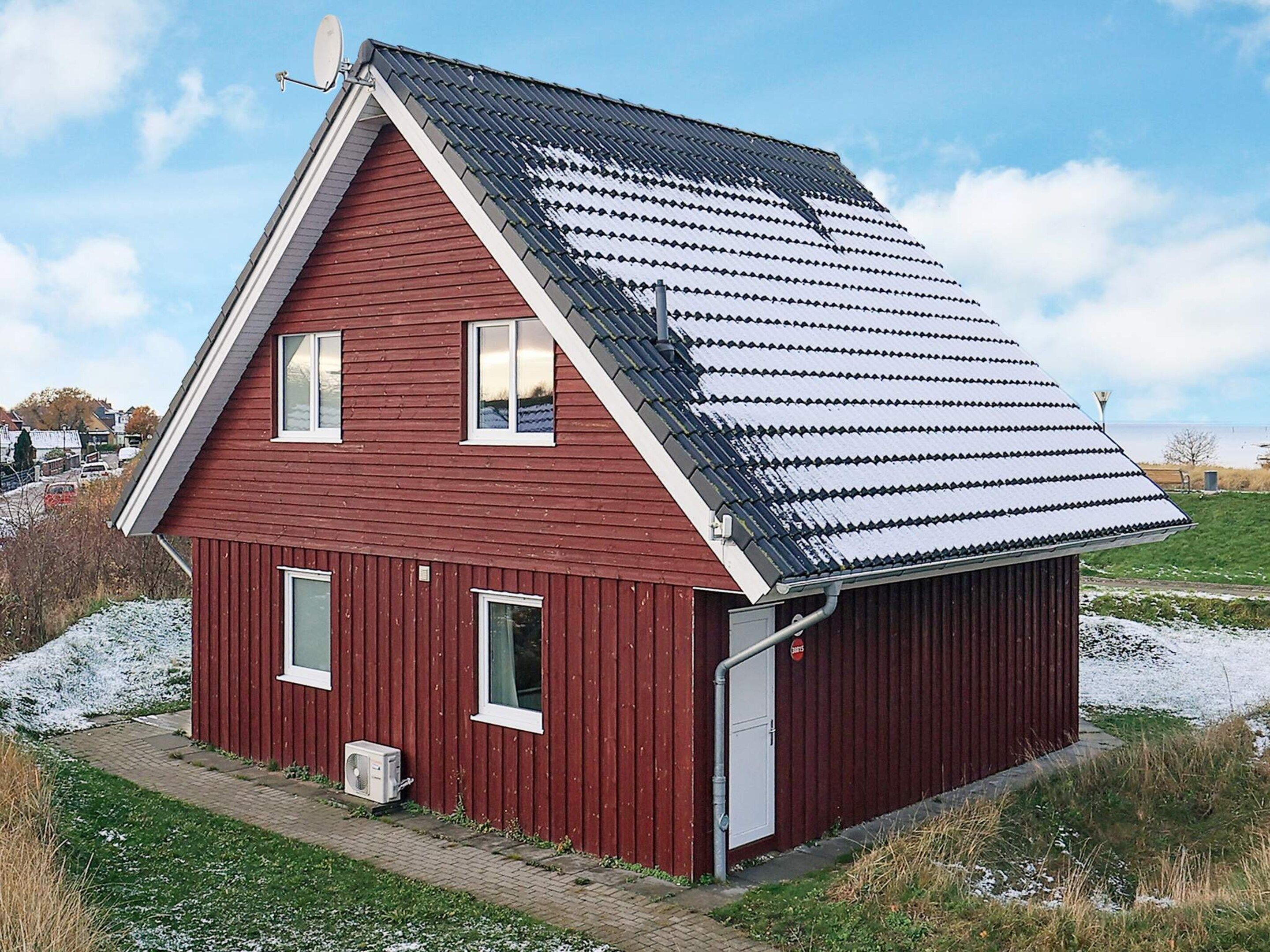 Une maison en bois rouge, avec un toit en pente, un garage et une antenne parabolique bien visible.