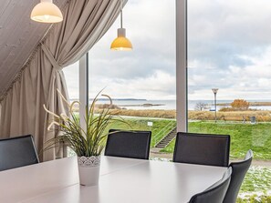 Ein Essbereich mit Tisch, Stühlen, einer Topfpflanze und Blick auf eine grüne Landschaft durch große Fenster.