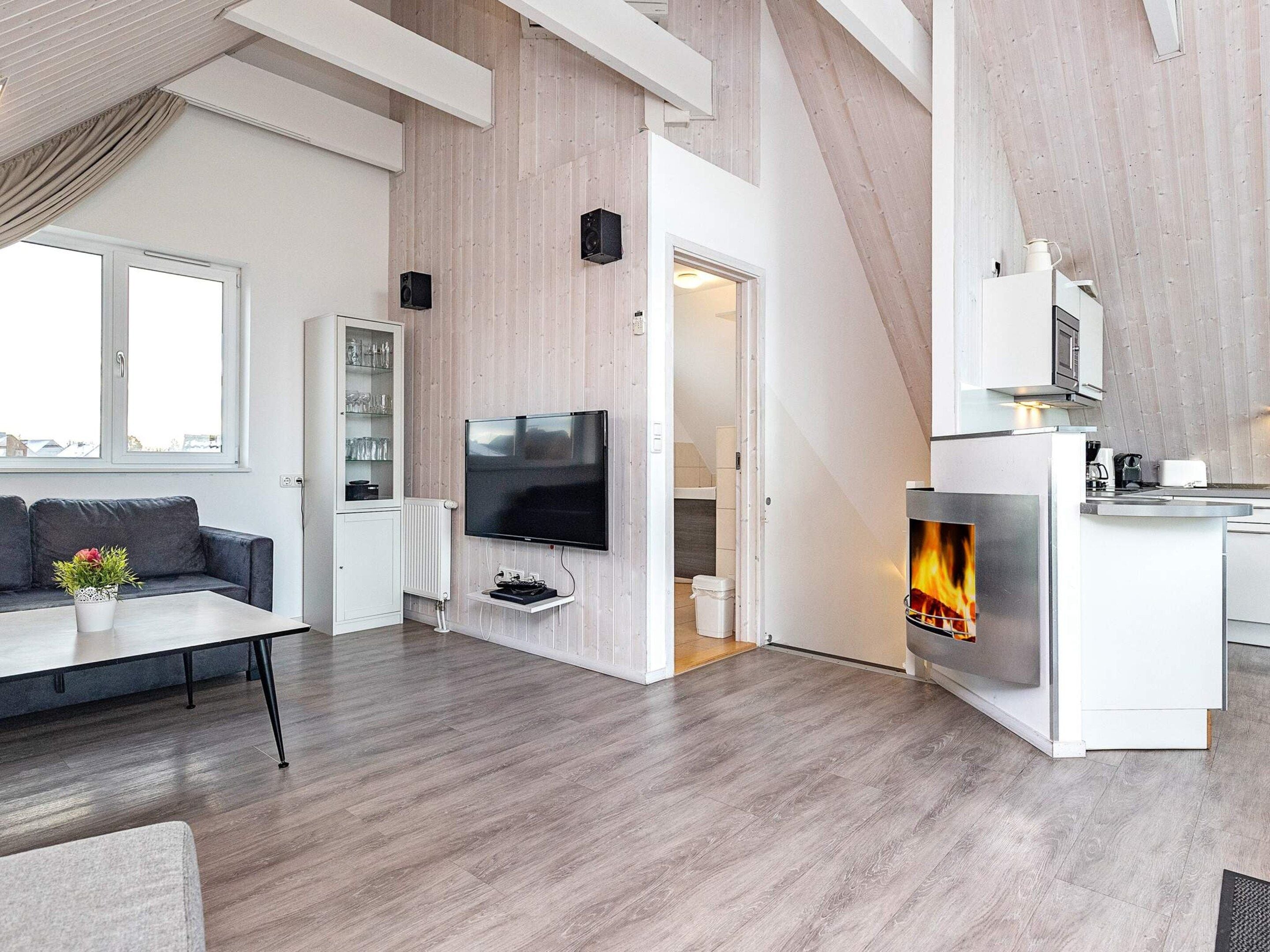 A modern living room with a flat-screen TV, a fireplace, a sofa, and a kitchen area.