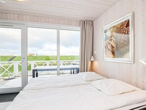 A bedroom with a large bed, a view of the beach, and a painting on the wall. - Holiday Home in Wendtorf (Wendtorf)