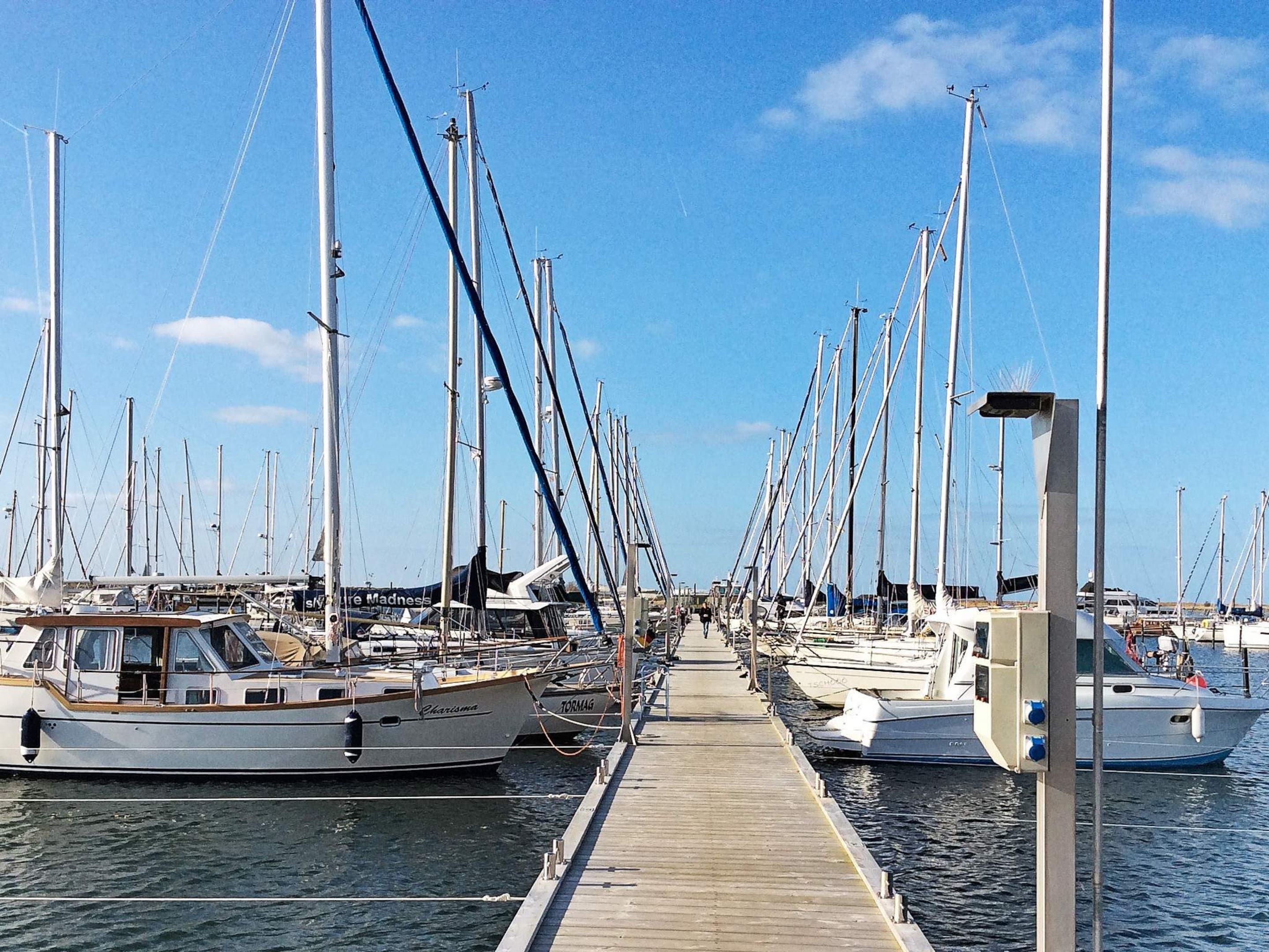 A marina with multiple boats docked along a wooden pier.