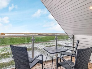 An outdoor patio with a table and chairs, overlooking a grassy field and a distant industrial area. - Holiday Home in Wendtorf (Wendtorf)