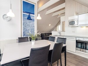 A modern kitchen with a microwave, stove, and sink. There is a dining area with a table and chairs, and a potted plant on the table. - Holiday Home in Wendtorf (Wendtorf)