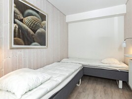 Un dormitorio con dos camas individuales, una mesita de noche con lámpara y un cuadro enmarcado en la pared.