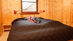 Una habitación con cama, paredes de madera, una ventana y una mesita de noche.