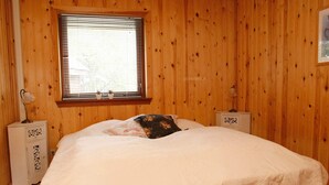 A bedroom with a wooden paneled wall, a bed with a white bedspread, two bedside tables with lamps, and a window with blinds. - 4 Star Holiday Home in Hals (Hals)