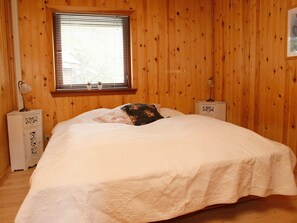 A bedroom with a wooden paneled wall, a bed with a white bedspread, two bedside tables with lamps, and a window with blinds. - 4 Star Holiday Home in Hals (Hals)