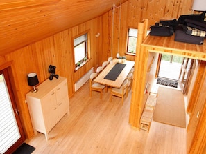 A wooden cabin interior with a dining table, chairs, a small cabinet, and a loft bed area.