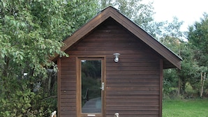 A small wooden cabin with a door and a light fixture above it, surrounded by greenery. - 4 Star Holiday Home in Hals (Hals)