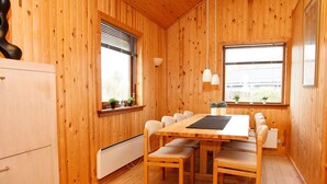 Una habitación con paneles de madera, una mesa de comedor, sillas, un radiador y ventanas con persianas.