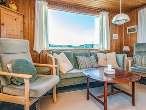 A cozy room with a wooden interior, a sofa, a chair, a table, and a window offering a view.