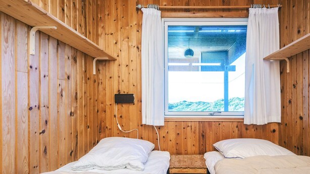 A wooden room with two beds, a window with curtains, and a small wooden table. - 6 Person Holiday Home in Henne (Henne)