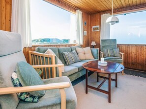 A cozy cabin interior with a wooden ceiling, a sofa, two armchairs, a small table, and a view of the outdoors. - 6 Person Holiday Home in Henne (Henne)
