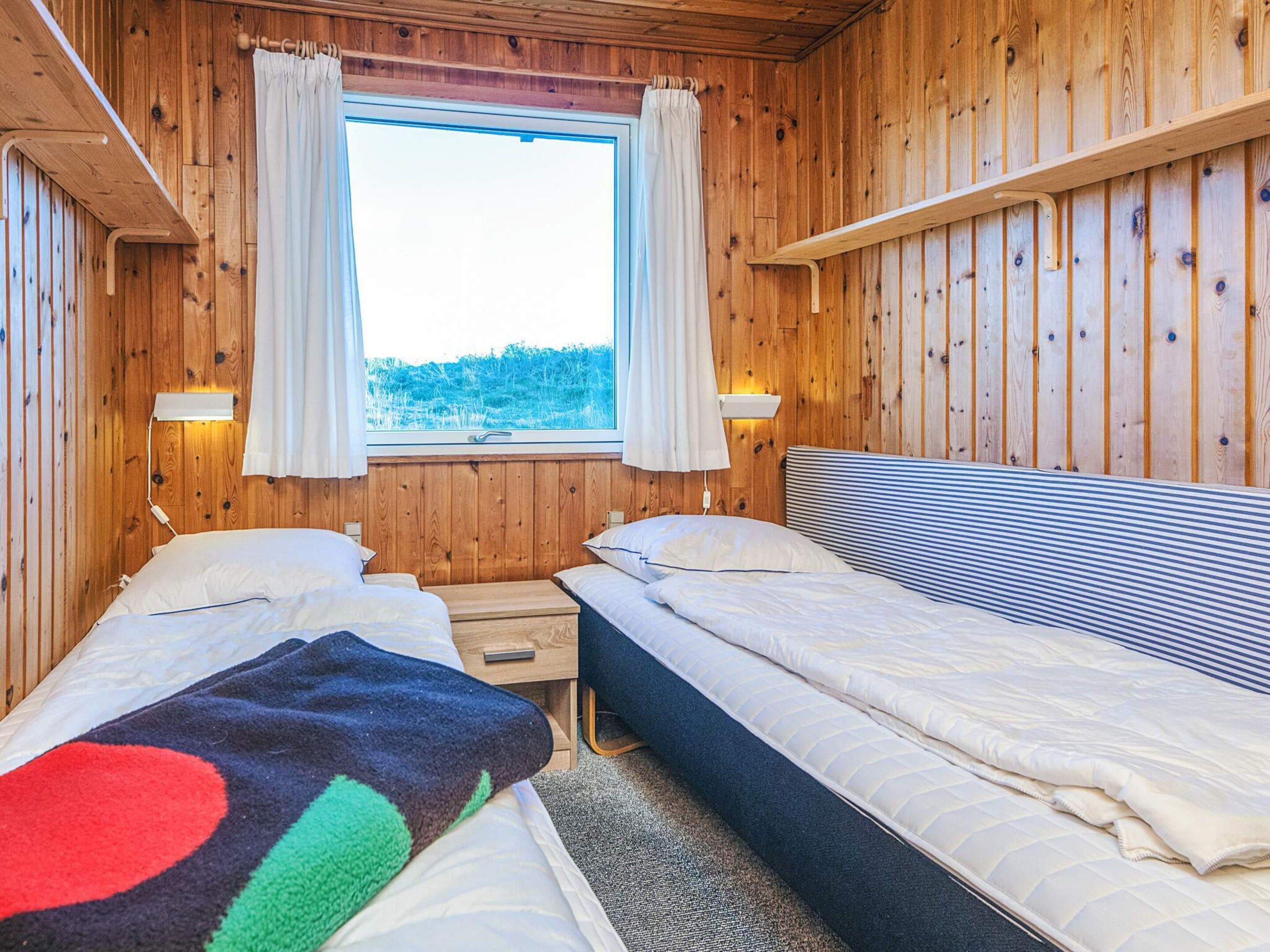 A wooden cabin room with two beds, a window with curtains, and a nightstand.