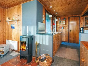 A cozy cabin interior with a wood stove, a small kitchen area, and a wooden ceiling. - 6 Person Holiday Home in Henne (Henne)