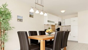 A dining area with a wooden table and black chairs, a potted plant, and a kitchen in the background. - Holiday Home in Grossenbrode (Grossenbrode)