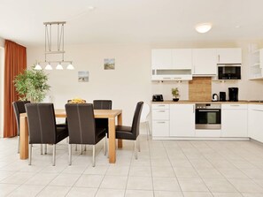 A modern kitchen with white cabinets, a microwave, and an oven. There is a dining table with chairs and a plant. - Holiday Home in Grossenbrode (Grossenbrode)