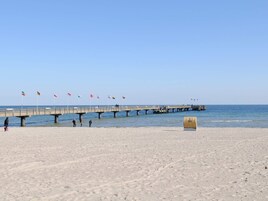 A beach with a pier extending into the water, flags, and a trash bin.