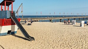 A beach with a lifeguard tower, a pier, and flags. - Holiday Home in Grossenbrode (Grossenbrode)