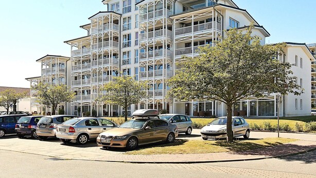 A multi-story residential building with balconies, parked cars, and a clear sky. - Holiday Home in Grossenbrode (Grossenbrode)