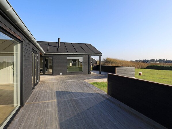A modern house with a large deck, a glass door entrance, and a view of the surrounding landscape.