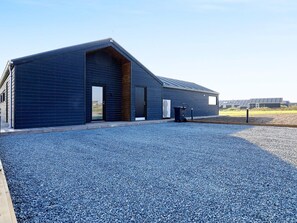 A modern building with a sloped roof, large windows, and a gravel driveway.