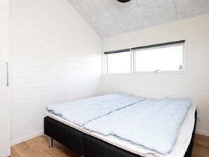 A single bed with a white mattress and a black headboard in a room with white walls and a sloped ceiling.