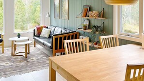 A cozy living room with a wooden dining table, a sofa, and a coffee table. There are framed pictures on the wall and a hanging light fixture. - 6 Person Holiday Home in Albaek-by Traum (Aalbaek)