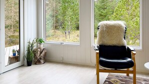 A room with a large window, a black leather chair with a fluffy white cushion, a patterned rug, and a small plant on a wooden stump. - 6 Person Holiday Home in Albaek-by Traum (Aalbaek)