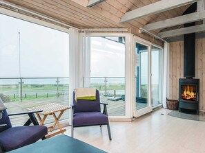 A room with a wooden ceiling, a fireplace, a table with chairs, and a view of the outdoors.