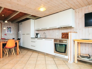 A modern kitchen with white cabinets, a stainless steel oven, and a dining area with a wooden table and orange chairs.