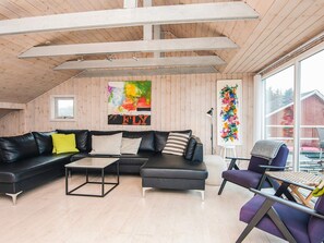 En moderne stue i loftstil med en sort lædersofa, et lille sofabord og en lilla lænestol. To store vinduer giver naturligt lys og udsigt ud.